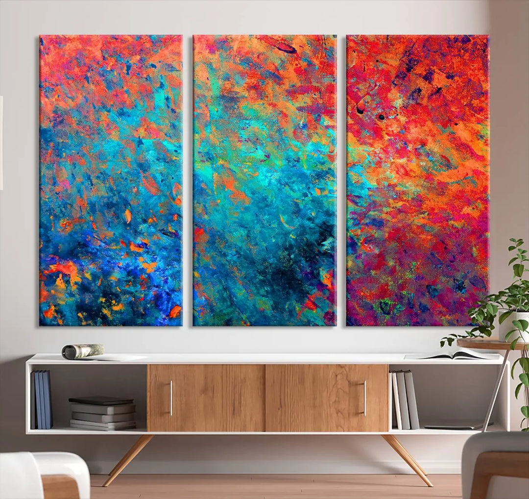 A three-part Colorful Abstract Canvas Wall Art Print, featuring vivid splashes of blue, orange, and red, is showcased on gallery-wrapped, museum-quality canvas with a UV-protective coating.