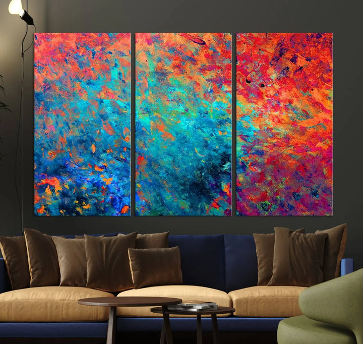 A three-part Colorful Abstract Canvas Wall Art Print, featuring vivid splashes of blue, orange, and red, is showcased on gallery-wrapped, museum-quality canvas with a UV-protective coating.