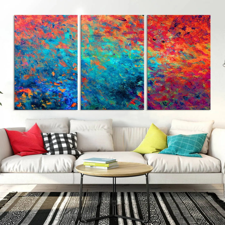 A three-part Colorful Abstract Canvas Wall Art Print, featuring vivid splashes of blue, orange, and red, is showcased on gallery-wrapped, museum-quality canvas with a UV-protective coating.