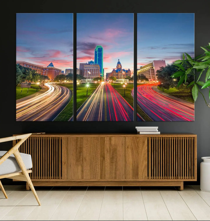 A modern living room features a cityscape triptych wall art titled "Dallas City Street Lights Sunset Pink Cloudy Skyline Cityscape View," printed on museum-quality canvas. It captures a vibrant evening skyline with light trails.