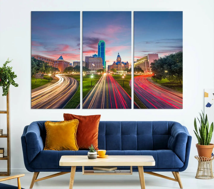 A modern living room features a cityscape triptych wall art titled "Dallas City Street Lights Sunset Pink Cloudy Skyline Cityscape View," printed on museum-quality canvas. It captures a vibrant evening skyline with light trails.