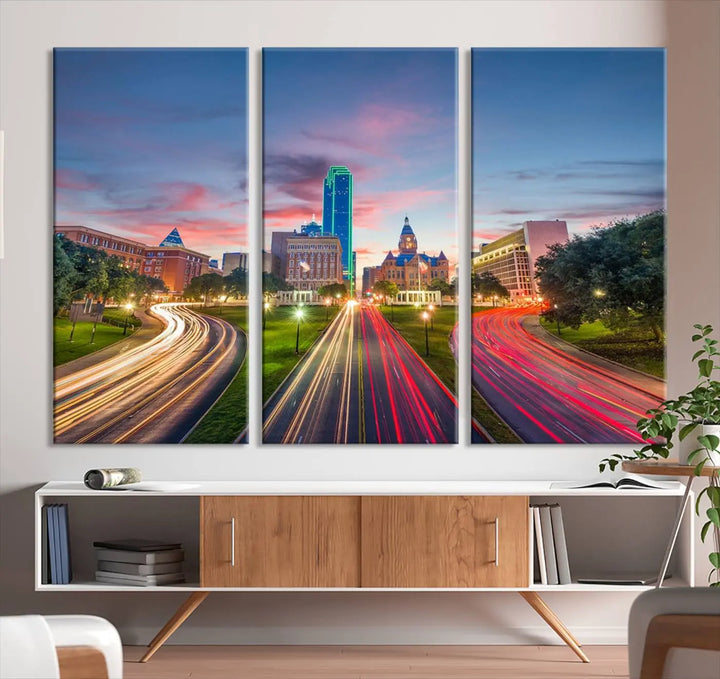 A modern living room features a cityscape triptych wall art titled "Dallas City Street Lights Sunset Pink Cloudy Skyline Cityscape View," printed on museum-quality canvas. It captures a vibrant evening skyline with light trails.