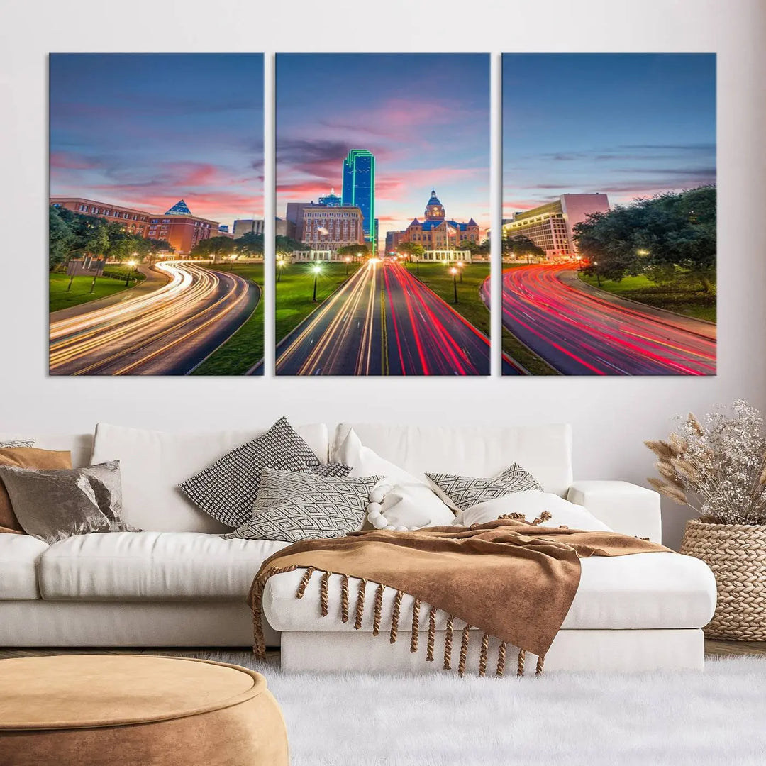 A modern living room features a cityscape triptych wall art titled "Dallas City Street Lights Sunset Pink Cloudy Skyline Cityscape View," printed on museum-quality canvas. It captures a vibrant evening skyline with light trails.