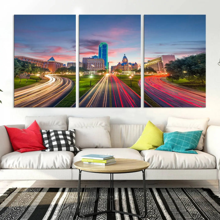 A modern living room features a cityscape triptych wall art titled "Dallas City Street Lights Sunset Pink Cloudy Skyline Cityscape View," printed on museum-quality canvas. It captures a vibrant evening skyline with light trails.