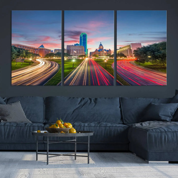 A modern living room features a cityscape triptych wall art titled "Dallas City Street Lights Sunset Pink Cloudy Skyline Cityscape View," printed on museum-quality canvas. It captures a vibrant evening skyline with light trails.