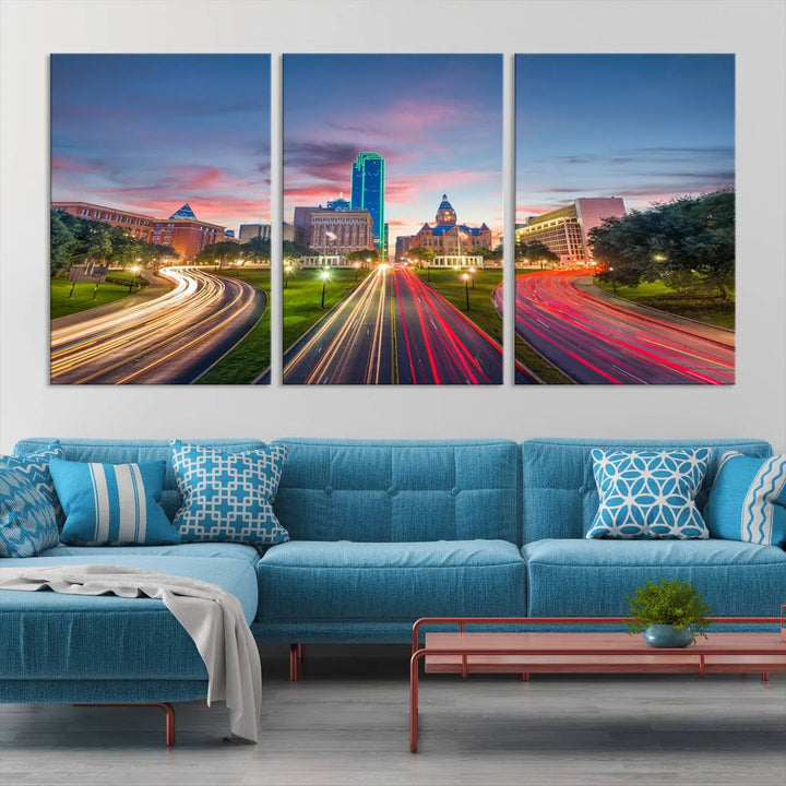 A modern living room features a cityscape triptych wall art titled "Dallas City Street Lights Sunset Pink Cloudy Skyline Cityscape View," printed on museum-quality canvas. It captures a vibrant evening skyline with light trails.