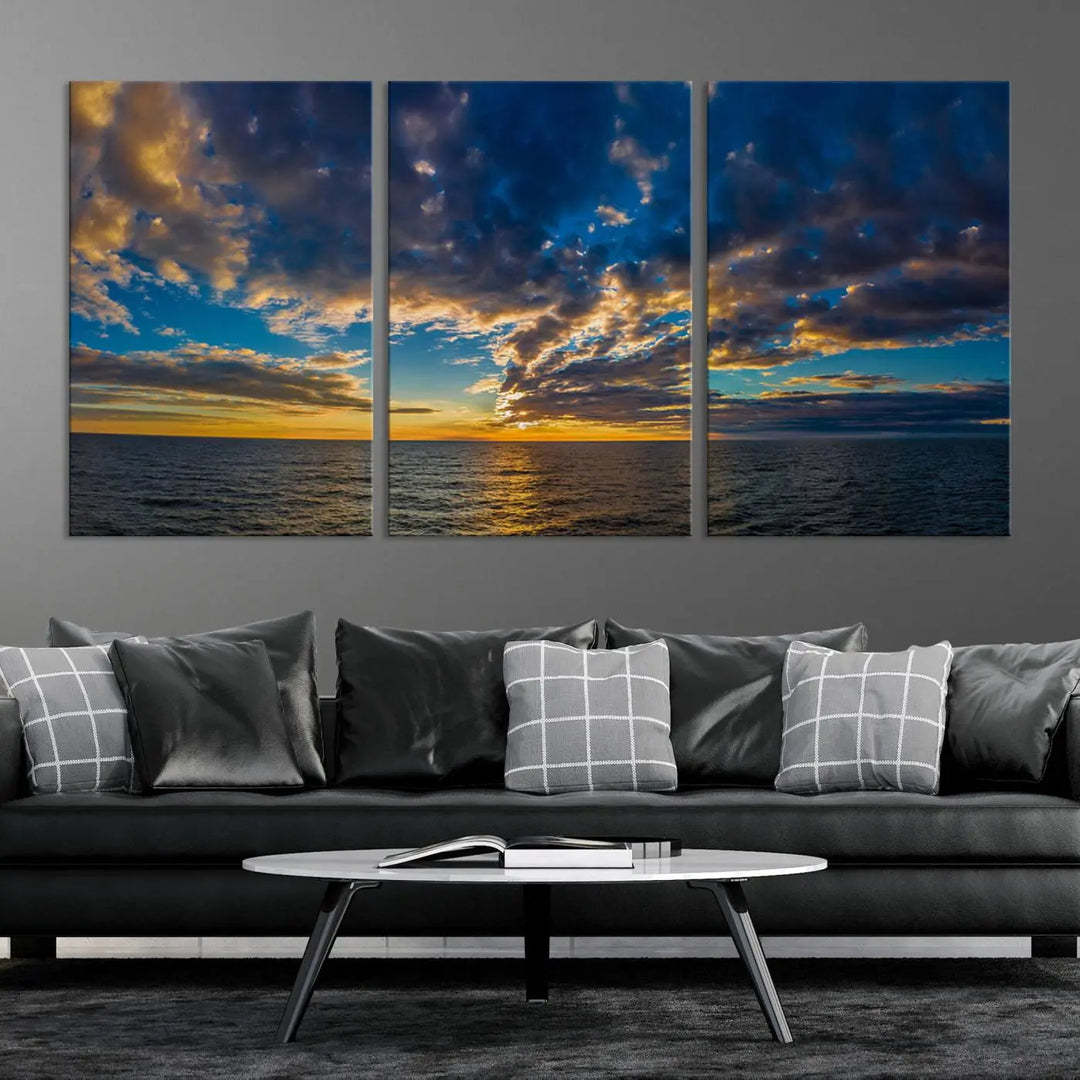 In a cozy living room, the Dark Clouds on the Ocean Beach Sunset Wall Art Canvas Print, featuring three panels and a museum-quality finish, hangs prominently.