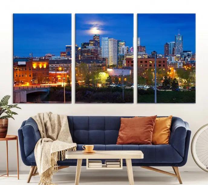 A triptych of the "Denver City Lights Night Blue Skyline Cityscape View" wall art canvas print enhances a modern living room. Crafted on museum-quality canvas with a UV-protective coating, this artwork is ready to hang and effortlessly elevate your space.