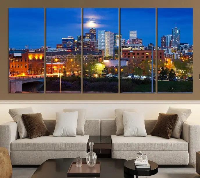 A triptych of the "Denver City Lights Night Blue Skyline Cityscape View" wall art canvas print enhances a modern living room. Crafted on museum-quality canvas with a UV-protective coating, this artwork is ready to hang and effortlessly elevate your space.