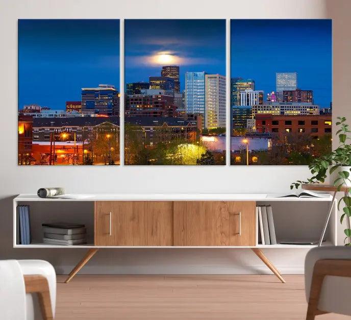 The Denver City Lights Night Blue Skyline Cityscape View Wall Art Canvas Print captures a stunning skyline at night with illuminated buildings and a bright moon, presented on gallery-quality canvas for an elegant display.