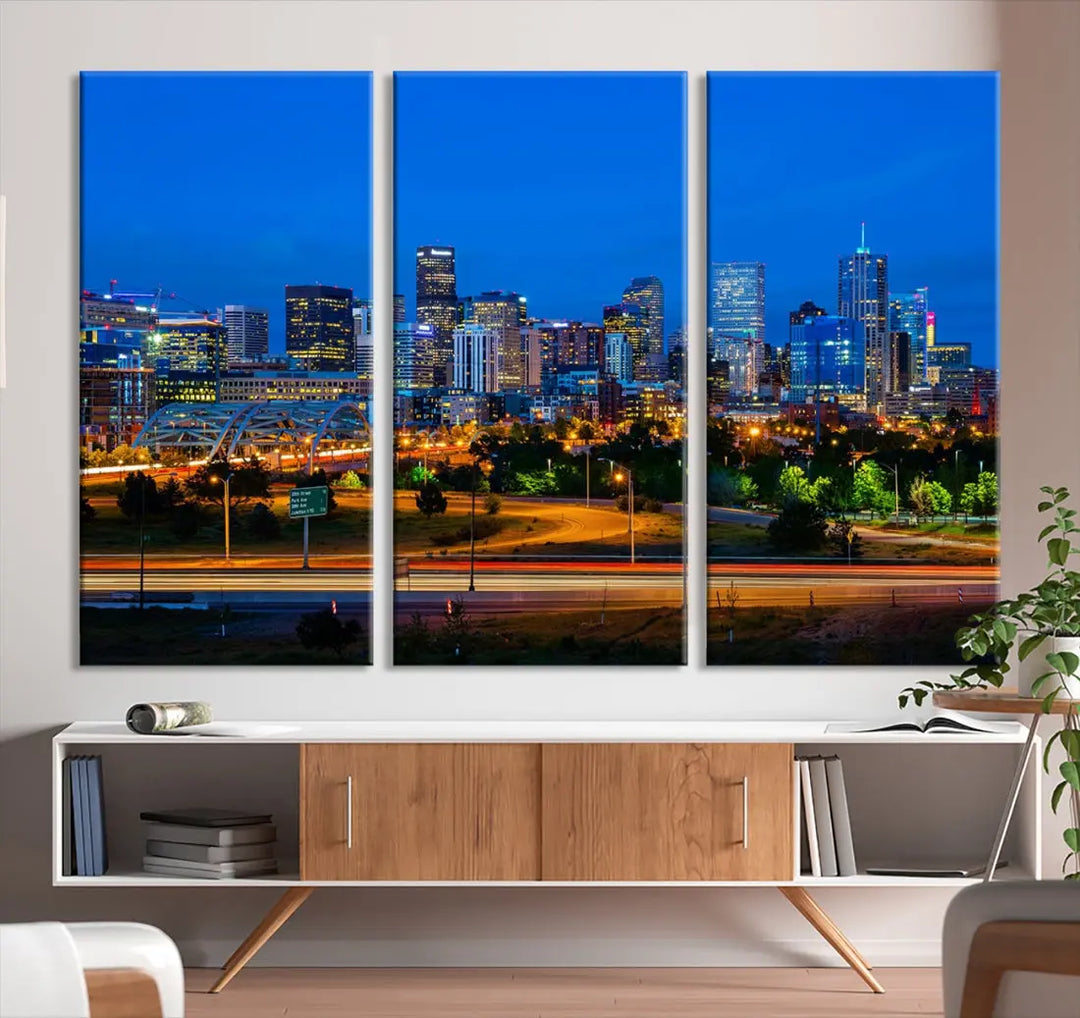 A modern living room showcases the "Denver City Lights Night Blue Skyline Cityscape View Wall Art Canvas Print" in a triptych arrangement. These museum-quality canvases, finished with a UV-protective coating, maintain their vibrant allure.