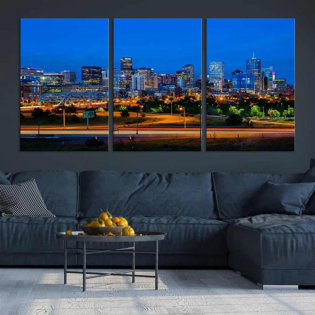 A modern living room showcases the "Denver City Lights Night Blue Skyline Cityscape View Wall Art Canvas Print" in a triptych arrangement. These museum-quality canvases, finished with a UV-protective coating, maintain their vibrant allure.