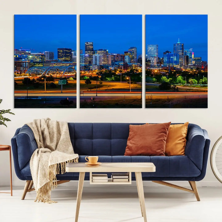 A modern living room showcases the "Denver City Lights Night Blue Skyline Cityscape View Wall Art Canvas Print" in a triptych arrangement. These museum-quality canvases, finished with a UV-protective coating, maintain their vibrant allure.