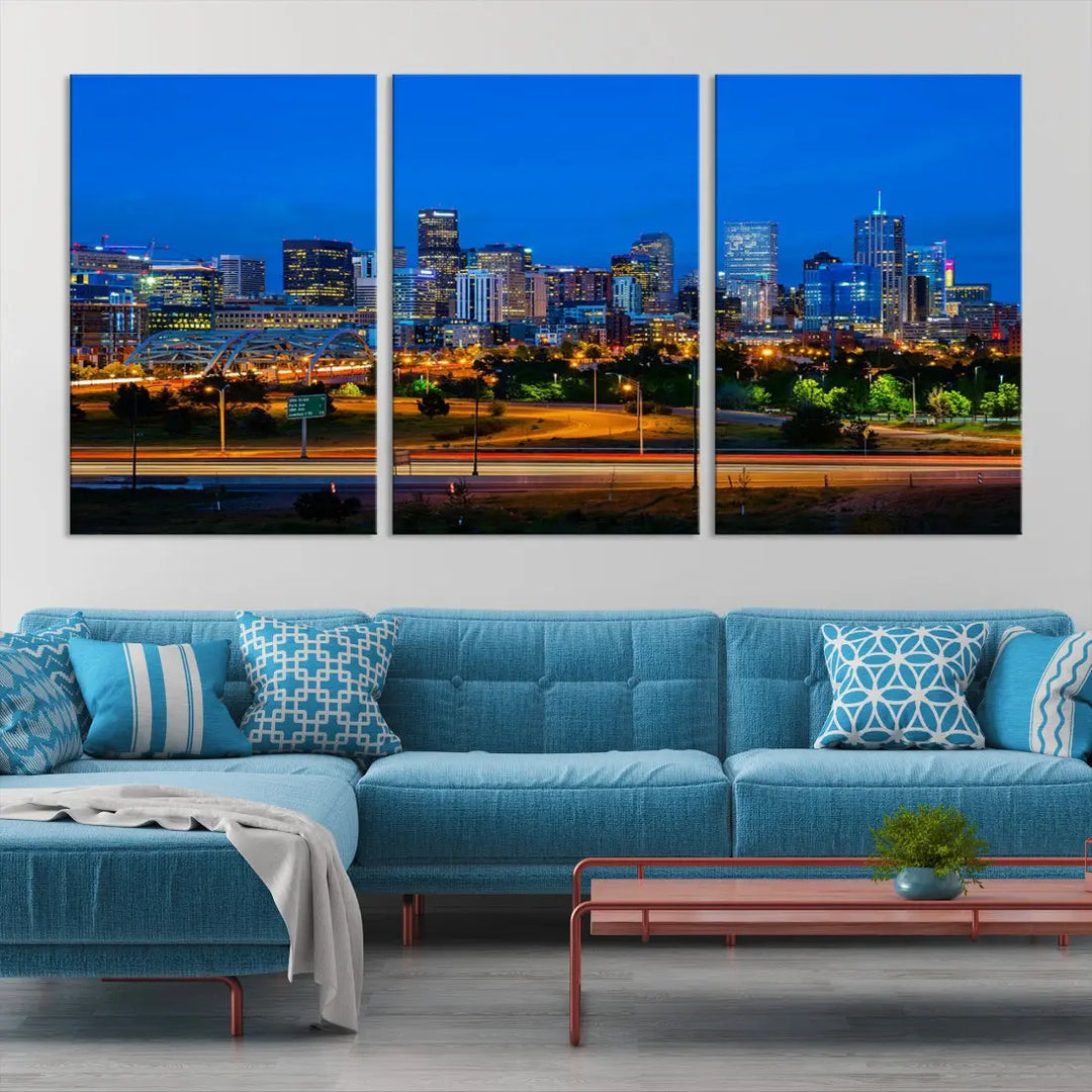 A modern living room showcases the "Denver City Lights Night Blue Skyline Cityscape View Wall Art Canvas Print" in a triptych arrangement. These museum-quality canvases, finished with a UV-protective coating, maintain their vibrant allure.