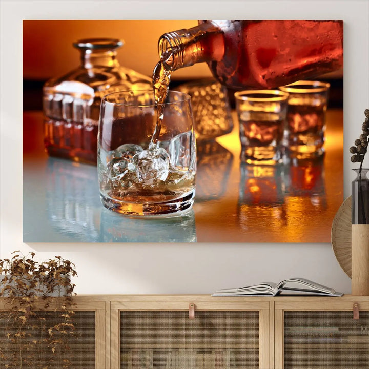 The Elegant Whiskey Canvas Art captures the reflection of a whiskey bottle pouring into an iced glass beside two filled ones.