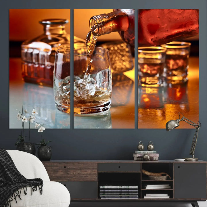 The Elegant Whiskey Canvas Art captures the reflection of a whiskey bottle pouring into an iced glass beside two filled ones.