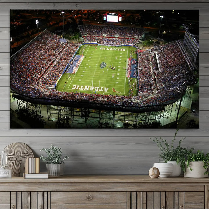 The wall art is a triptych canvas depicting the Florida Atlantic University Owls Football Team at the Boca Raton FAU Stadium, offering a gallery-quality finish.