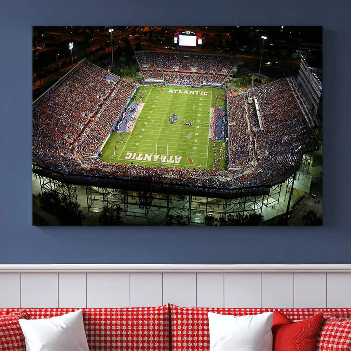 The wall art is a triptych canvas depicting the Florida Atlantic University Owls Football Team at the Boca Raton FAU Stadium, offering a gallery-quality finish.