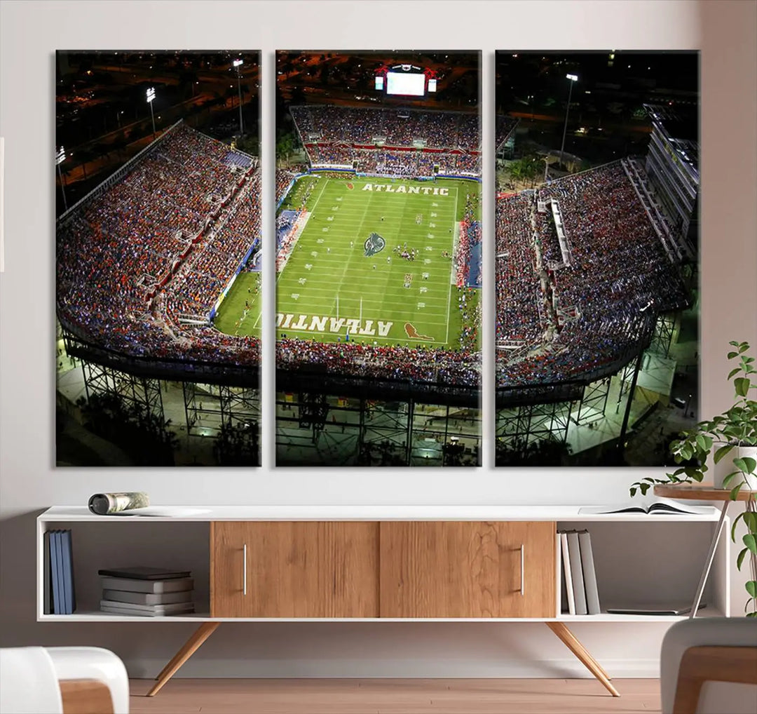 The wall art is a triptych canvas depicting the Florida Atlantic University Owls Football Team at the Boca Raton FAU Stadium, offering a gallery-quality finish.