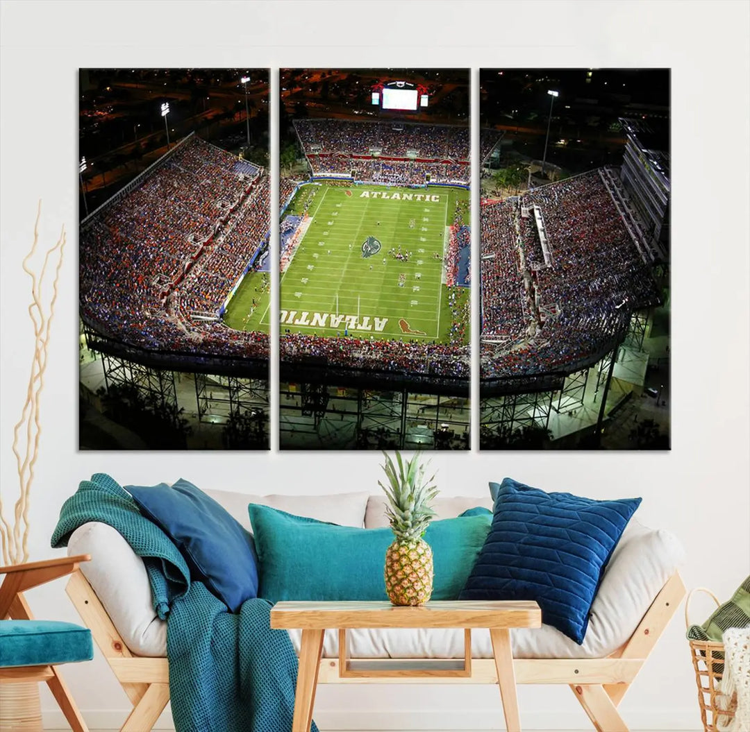 The wall art is a triptych canvas depicting the Florida Atlantic University Owls Football Team at the Boca Raton FAU Stadium, offering a gallery-quality finish.