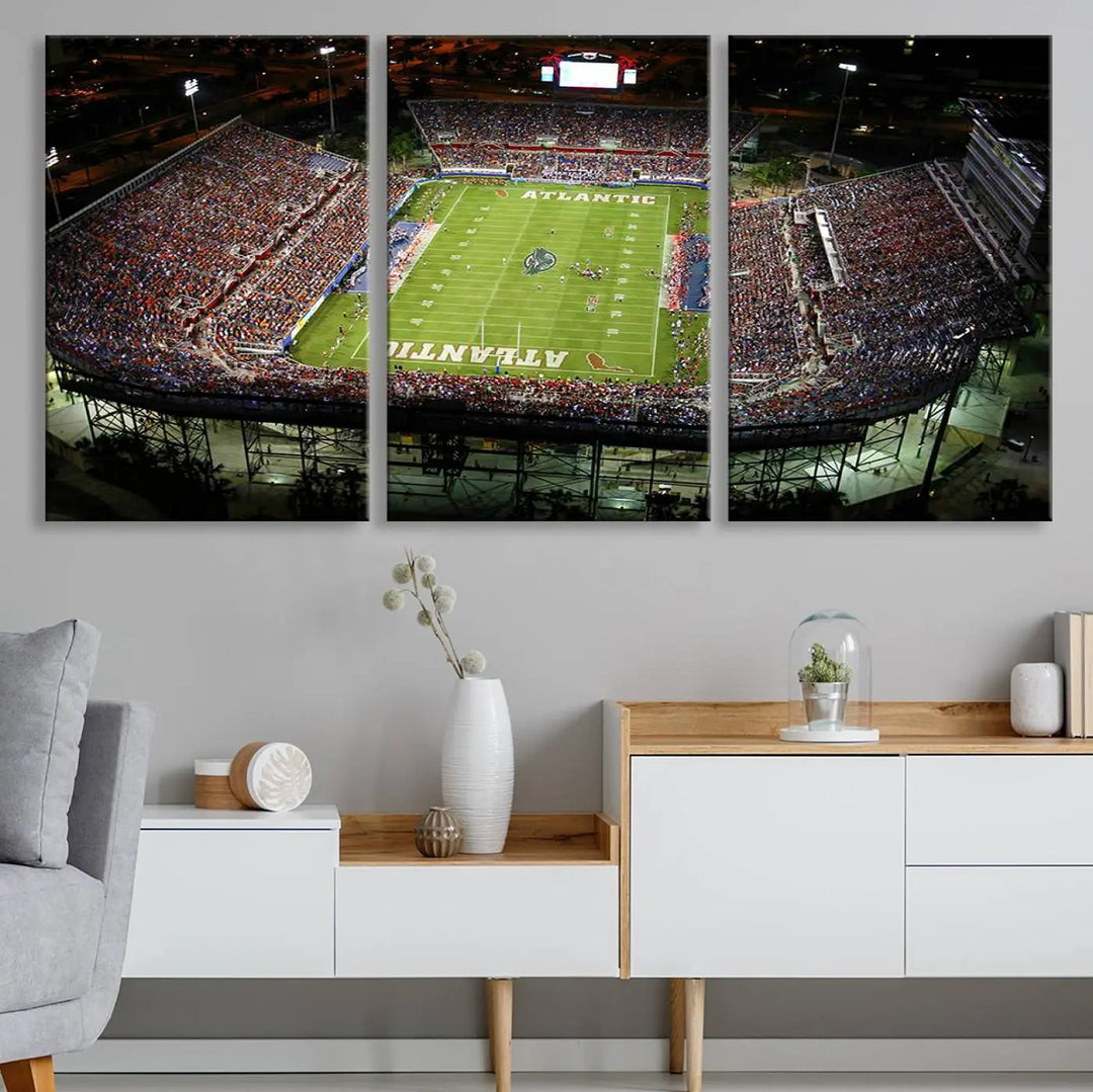 The wall art is a triptych canvas depicting the Florida Atlantic University Owls Football Team at the Boca Raton FAU Stadium, offering a gallery-quality finish.