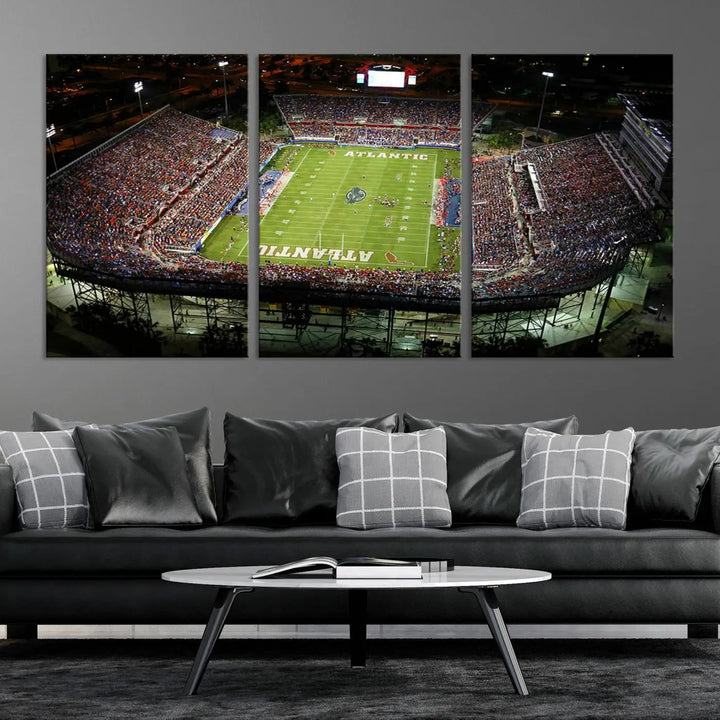 The wall art is a triptych canvas depicting the Florida Atlantic University Owls Football Team at the Boca Raton FAU Stadium, offering a gallery-quality finish.