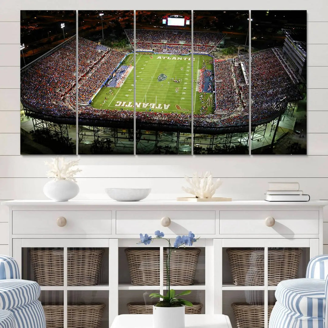 The wall art is a triptych canvas depicting the Florida Atlantic University Owls Football Team at the Boca Raton FAU Stadium, offering a gallery-quality finish.