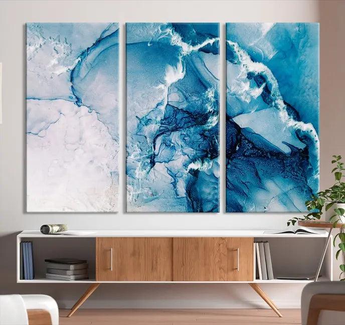 A set of Fluid Effect Wall Art Abstract Canvas prints, showcasing blue and white abstract designs on museum-quality canvas, is tastefully arranged on a dark wall.