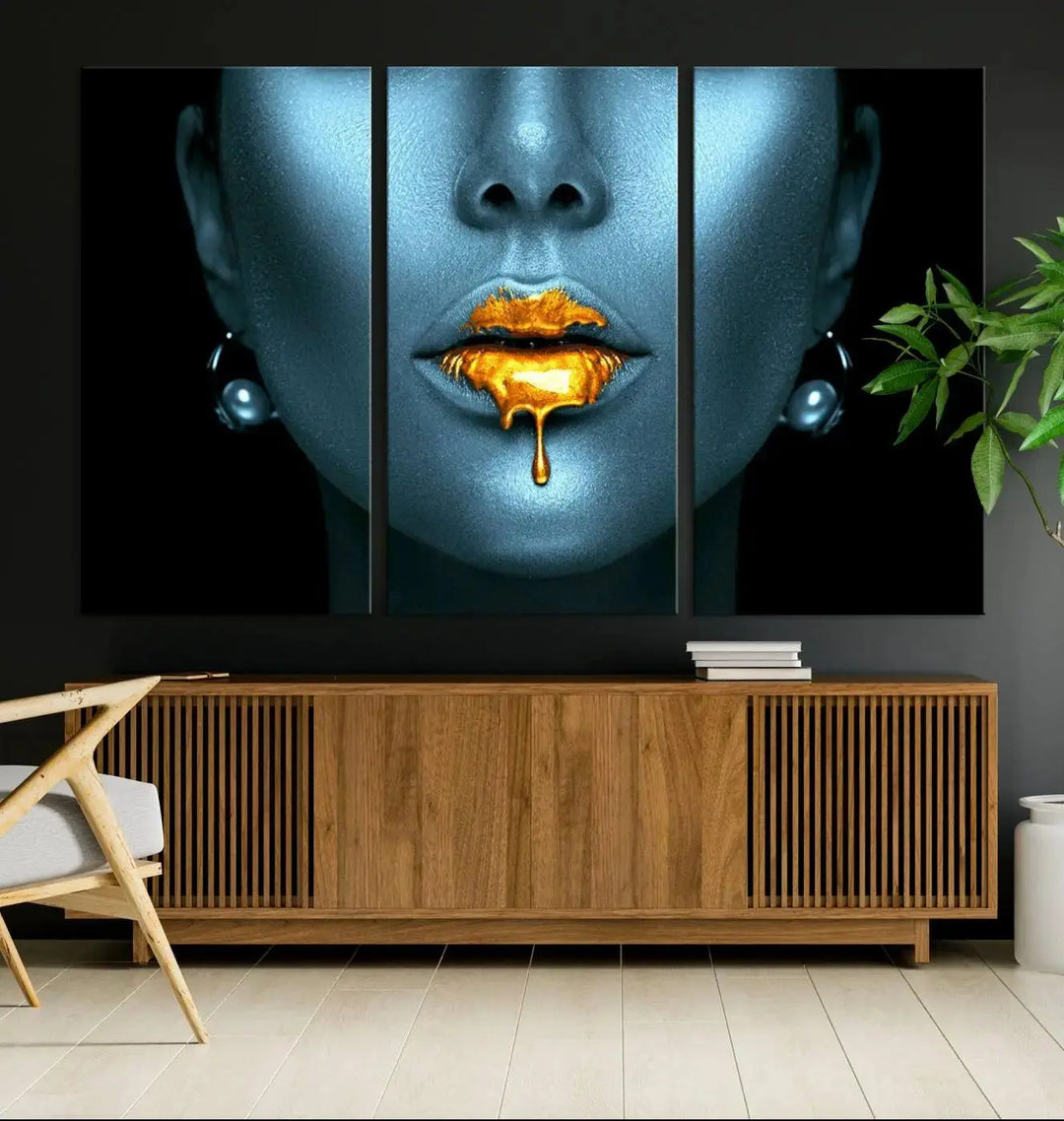 The Glitter Lips Wall Art Gold Lips Canvas Art Print in the contemporary living room showcases a blue-faced figure with glitter lips across three panels. The gallery-wrapped finish on high-quality polycotton canvas enhances the room's elegance.