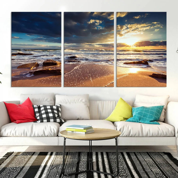 The cozy living room is enhanced by the Golden Hour Beach Sunset Canvas Triptych, featuring ocean waves and rocks.