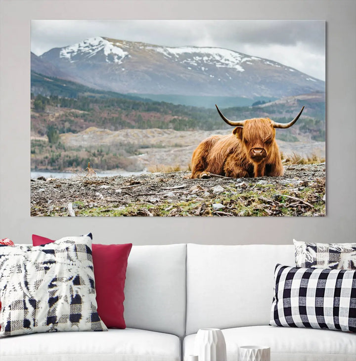 The Highland Cow Horn Farm Wall Art Canvas Print showcases a serene scene of a highland cow resting with snow-capped mountains in the background. This three-panel, museum-quality canvas features a UV-protective coating and is ready to hang.