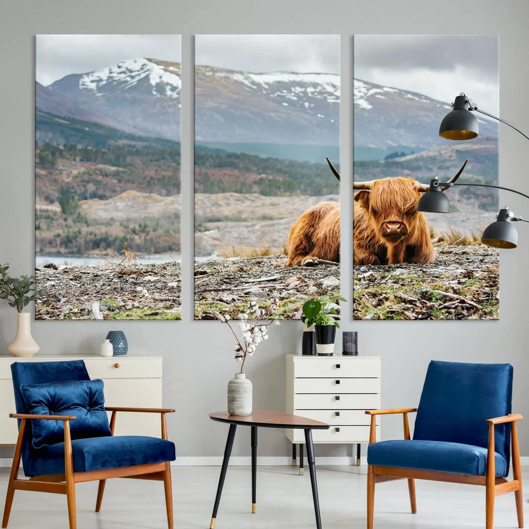 The Highland Cow Horn Farm Wall Art Canvas Print showcases a serene scene of a highland cow resting with snow-capped mountains in the background. This three-panel, museum-quality canvas features a UV-protective coating and is ready to hang.