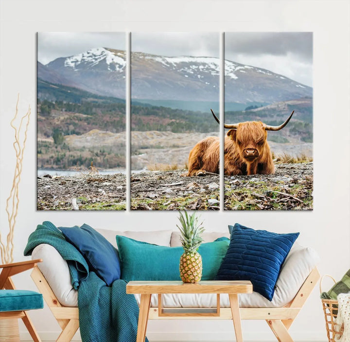 The Highland Cow Horn Farm Wall Art Canvas Print showcases a serene scene of a highland cow resting with snow-capped mountains in the background. This three-panel, museum-quality canvas features a UV-protective coating and is ready to hang.