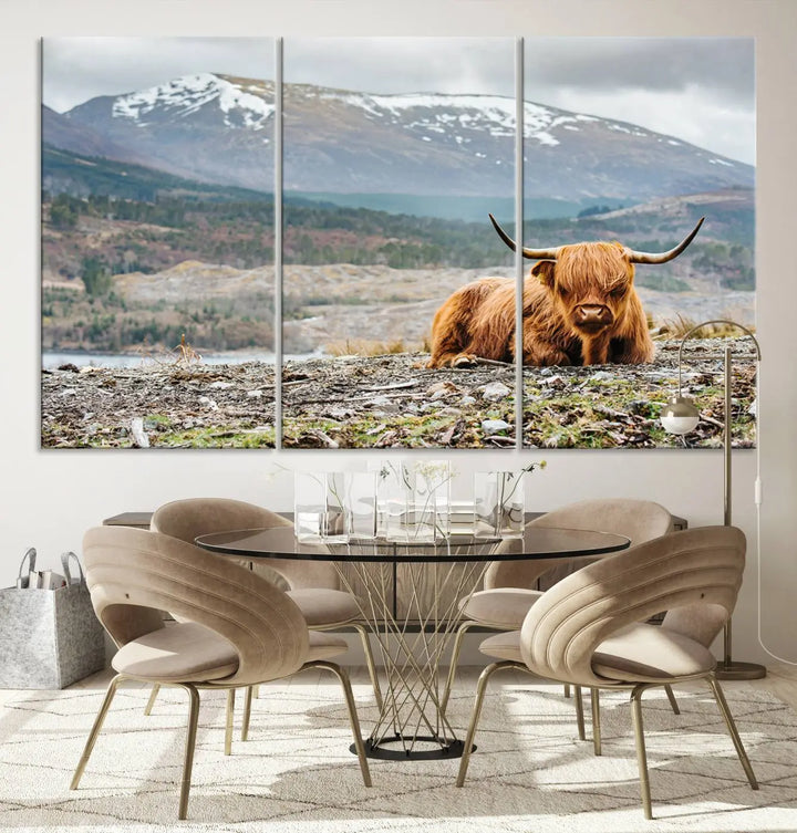 The Highland Cow Horn Farm Wall Art Canvas Print showcases a serene scene of a highland cow resting with snow-capped mountains in the background. This three-panel, museum-quality canvas features a UV-protective coating and is ready to hang.