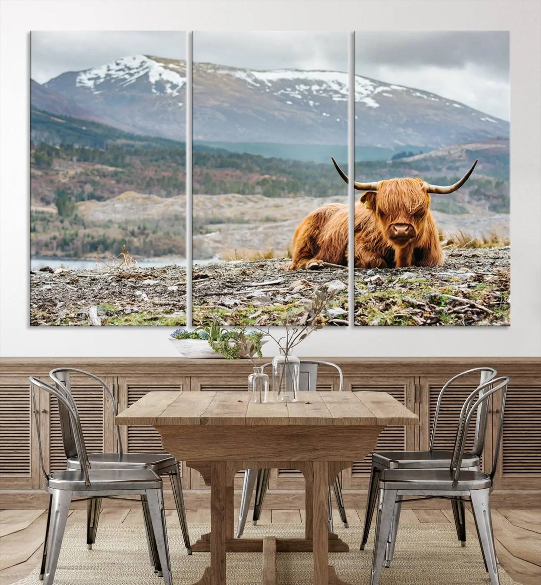 The Highland Cow Horn Farm Wall Art Canvas Print showcases a serene scene of a highland cow resting with snow-capped mountains in the background. This three-panel, museum-quality canvas features a UV-protective coating and is ready to hang.