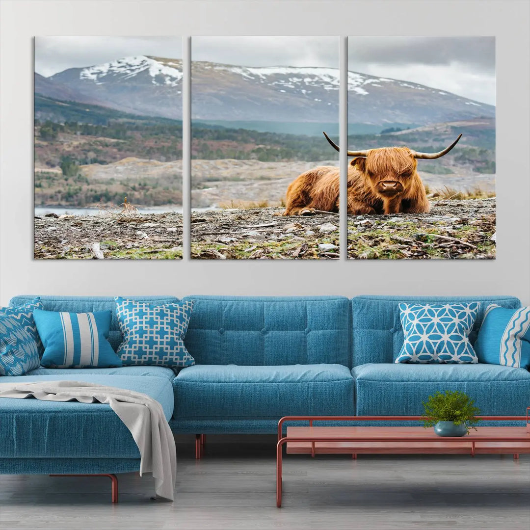 The Highland Cow Horn Farm Wall Art Canvas Print showcases a serene scene of a highland cow resting with snow-capped mountains in the background. This three-panel, museum-quality canvas features a UV-protective coating and is ready to hang.