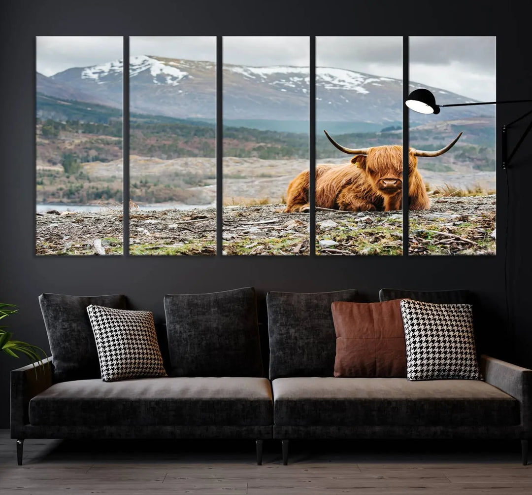 The Highland Cow Horn Farm Wall Art Canvas Print showcases a serene scene of a highland cow resting with snow-capped mountains in the background. This three-panel, museum-quality canvas features a UV-protective coating and is ready to hang.