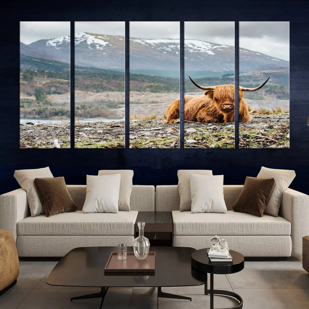 The Highland Cow Horn Farm Wall Art Canvas Print showcases a serene scene of a highland cow resting with snow-capped mountains in the background. This three-panel, museum-quality canvas features a UV-protective coating and is ready to hang.