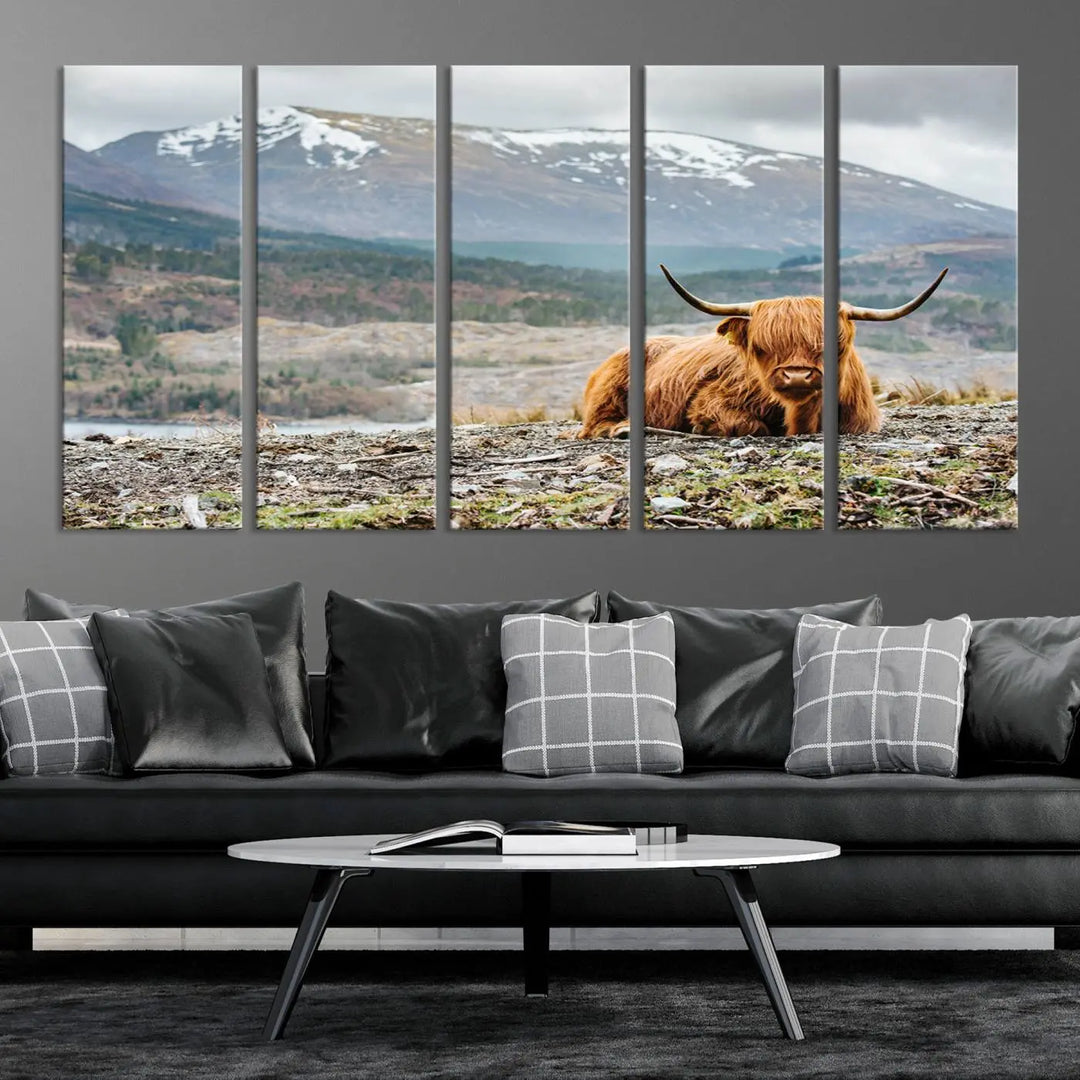 The Highland Cow Horn Farm Wall Art Canvas Print showcases a serene scene of a highland cow resting with snow-capped mountains in the background. This three-panel, museum-quality canvas features a UV-protective coating and is ready to hang.