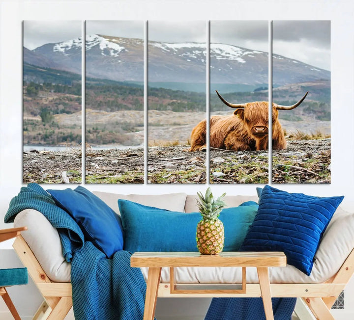 The Highland Cow Horn Farm Wall Art Canvas Print showcases a serene scene of a highland cow resting with snow-capped mountains in the background. This three-panel, museum-quality canvas features a UV-protective coating and is ready to hang.