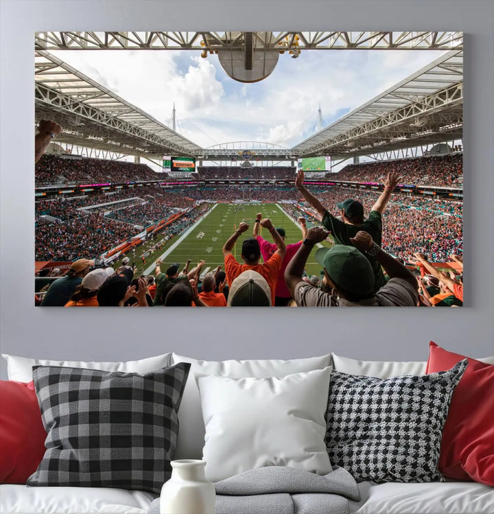 The living room features handmade triptych wall art crafted in the USA, depicting a cheering crowd at a Miami Hurricanes football game. The artwork showcases the Miami Hard Rock Stadium on premium canvas.