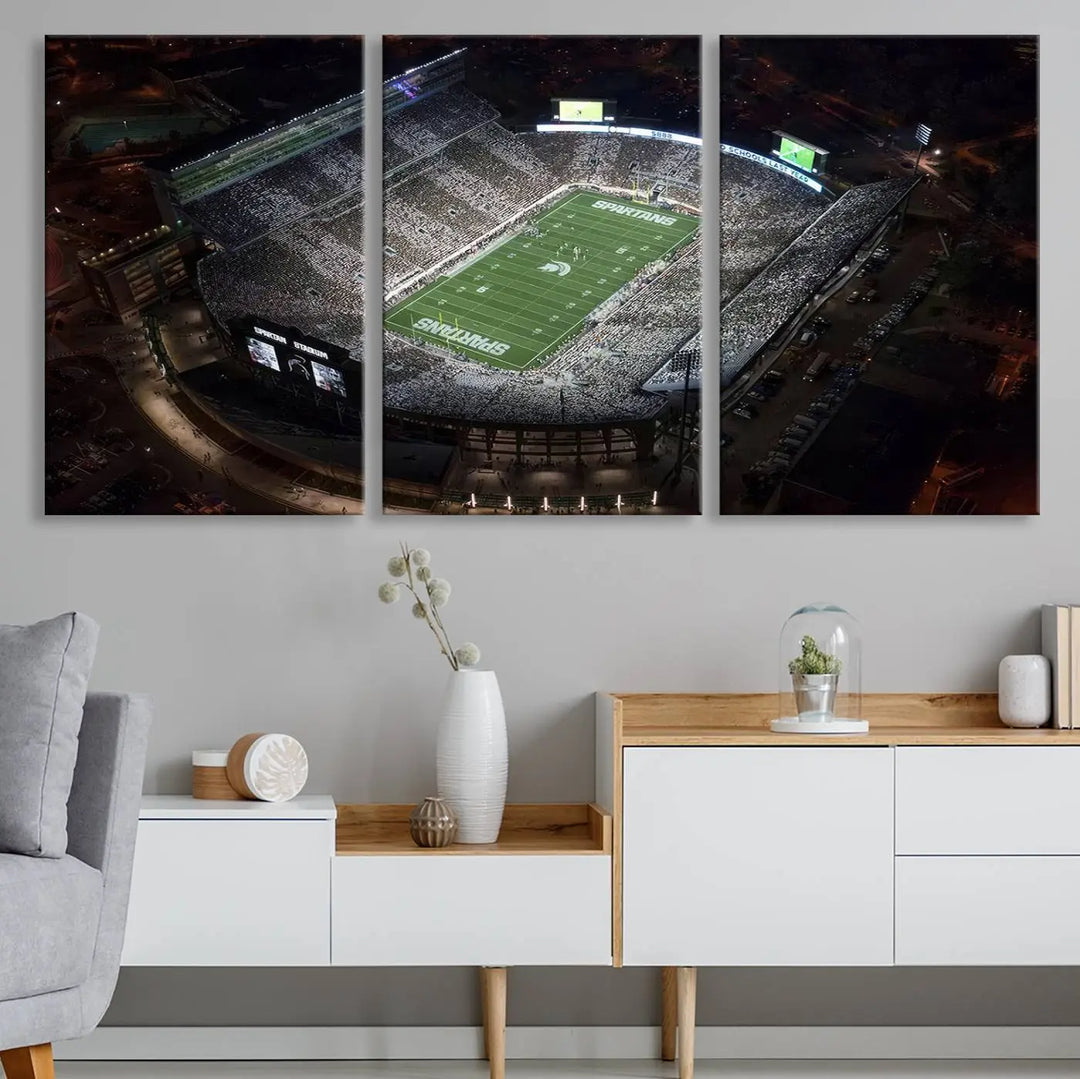 The "Michigan State Spartans Football Team Print - East Lansing Spartan Stadium Wall Art Canvas Print" is elegantly displayed on a wall, showcasing a brightly lit football stadium at night with a gallery-quality finish.