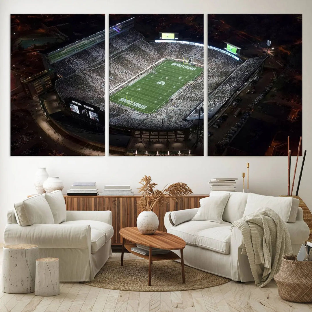 The "Michigan State Spartans Football Team Print - East Lansing Spartan Stadium Wall Art Canvas Print" is elegantly displayed on a wall, showcasing a brightly lit football stadium at night with a gallery-quality finish.