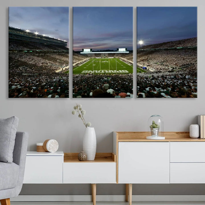 The living room features a Michigan State Spartans Football Team Print, a triptych canvas wall art depicting East Lansing's Spartan Stadium at dusk with a gallery-quality finish.