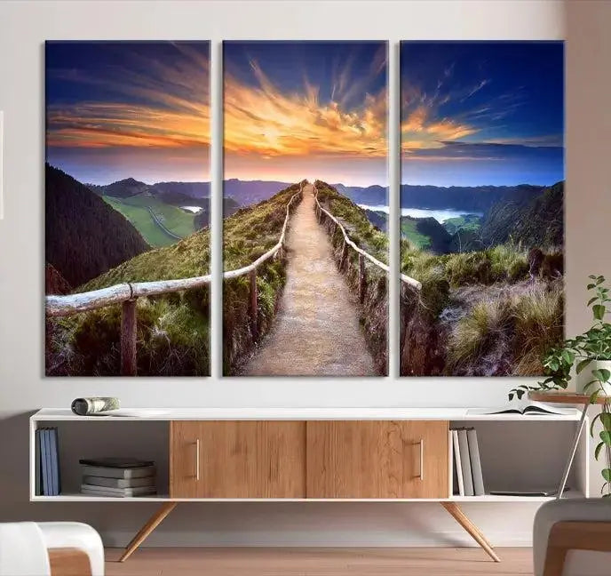 The Mountain and Sunset Wall Art Canvas Print, featuring a three-panel design on museum-quality canvas, captures a stunning sunset over a mountain path with a wooden railing. The hand-assembled frame ensures an exquisite finish and arrives ready to hang, adding natural beauty to any environment.