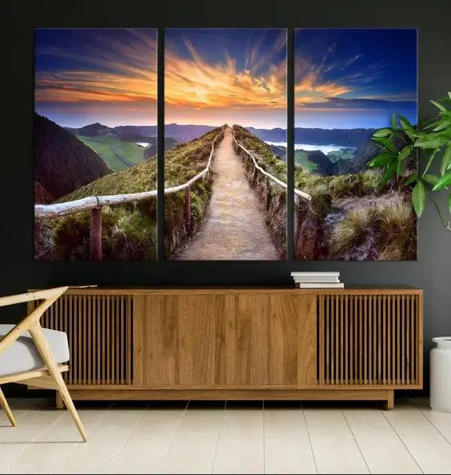 The Mountain and Sunset Wall Art Canvas Print, featuring a three-panel design on museum-quality canvas, captures a stunning sunset over a mountain path with a wooden railing. The hand-assembled frame ensures an exquisite finish and arrives ready to hang, adding natural beauty to any environment.