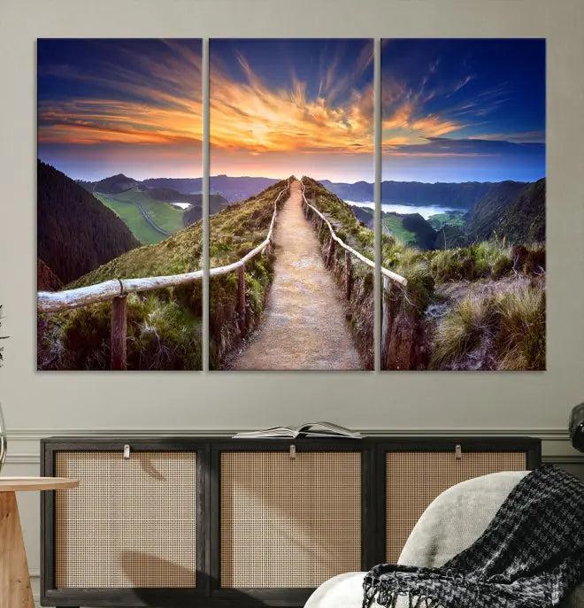 The Mountain and Sunset Wall Art Canvas Print, featuring a three-panel design on museum-quality canvas, captures a stunning sunset over a mountain path with a wooden railing. The hand-assembled frame ensures an exquisite finish and arrives ready to hang, adding natural beauty to any environment.