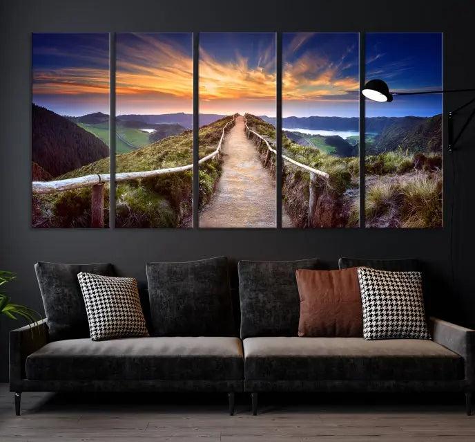 The Mountain and Sunset Wall Art Canvas Print, featuring a three-panel design on museum-quality canvas, captures a stunning sunset over a mountain path with a wooden railing. The hand-assembled frame ensures an exquisite finish and arrives ready to hang, adding natural beauty to any environment.