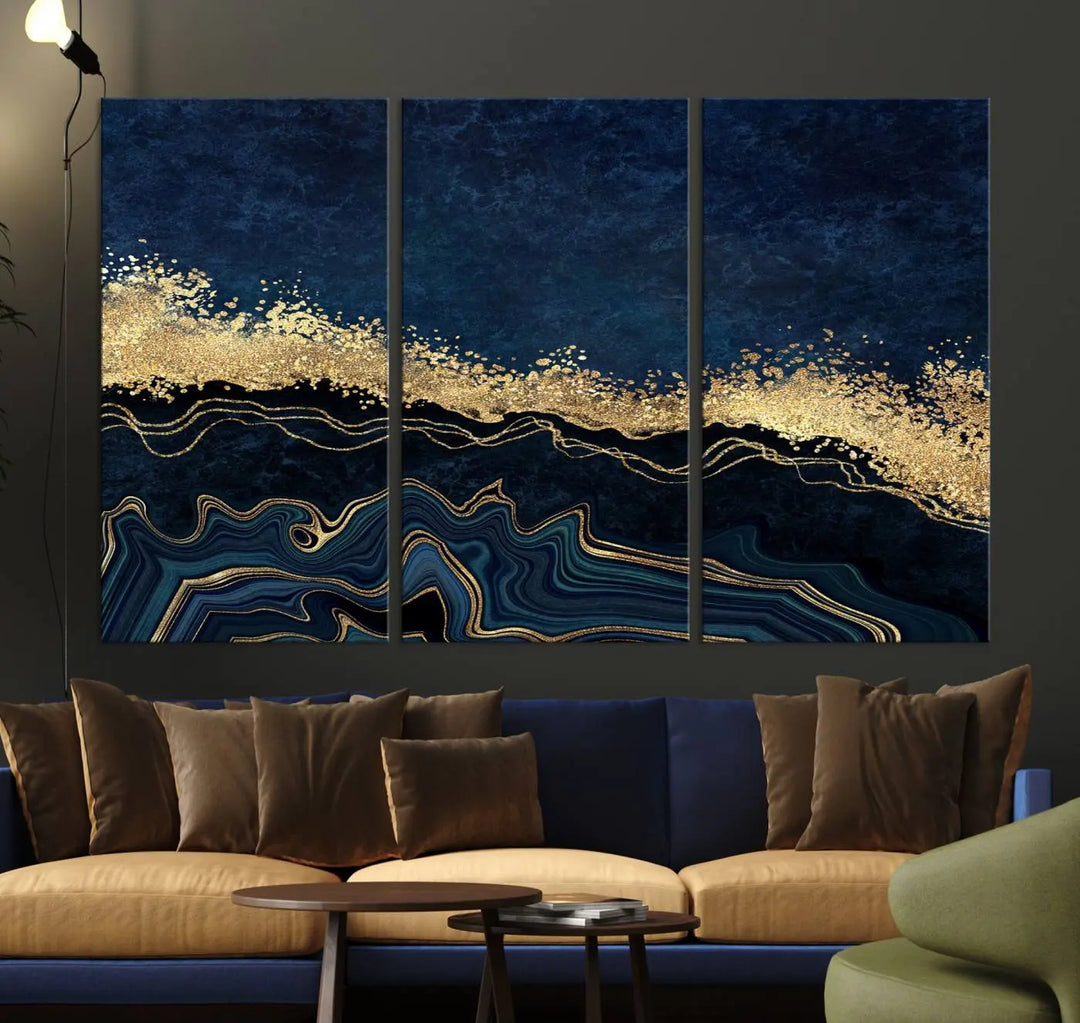 A modern living room featuring a ready-to-hang Navy Blue Marble Fluid Effect Large Wall Art, a stunning abstract triptych on museum-quality canvas in blue and gold. The artwork's vibrant colors are preserved with an enhanced UV-protective coating.