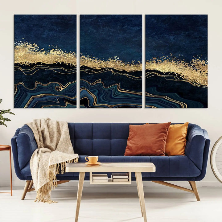 A modern living room featuring a ready-to-hang Navy Blue Marble Fluid Effect Large Wall Art, a stunning abstract triptych on museum-quality canvas in blue and gold. The artwork's vibrant colors are preserved with an enhanced UV-protective coating.